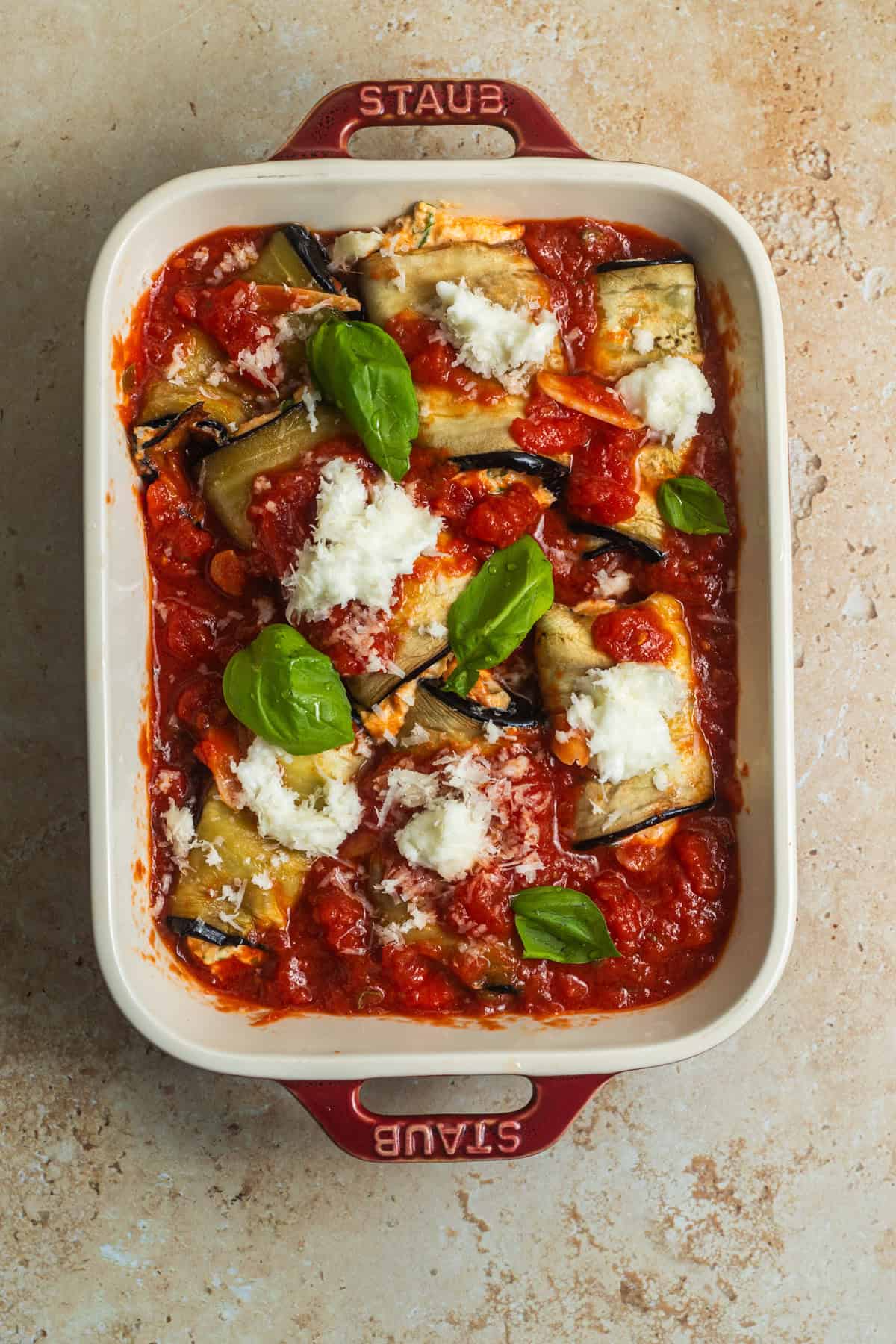 A casserole dish with layers of tomato sauce, eggplant roll-ups, mozzarella, and basil.