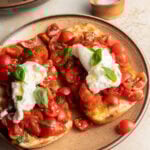A plate of bruschetta with cherry tomatoes and burrata, and a bowl of salt in the background.