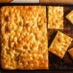 A large slab of focaccia on a metal baking sheet next to a few individual pieces.
