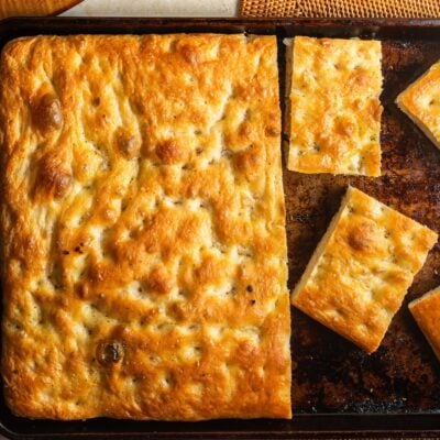 A large slab of focaccia on a metal baking sheet next to a few individual pieces.