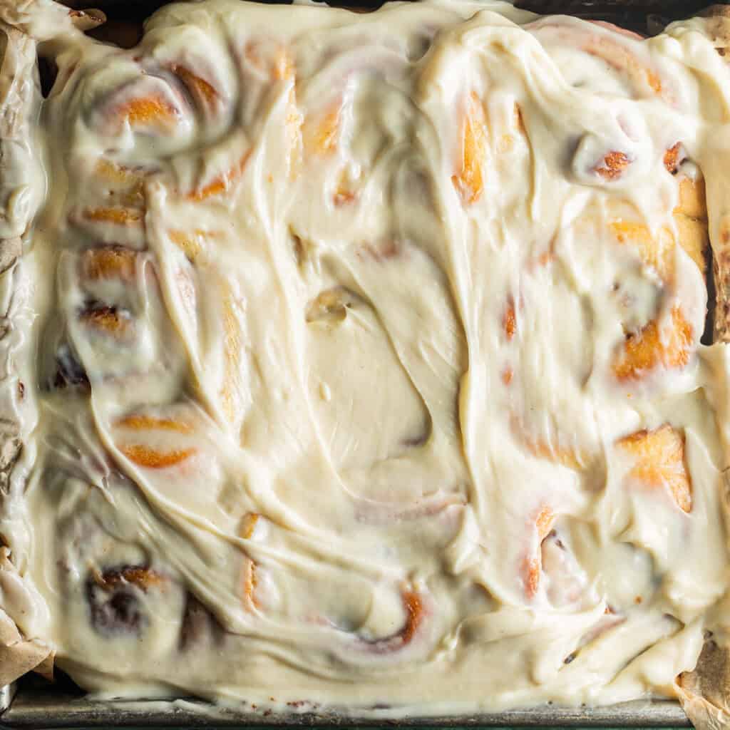 An 8x8 metal pan filled with cinnamon rolls glazed with cream cheese frosting.
