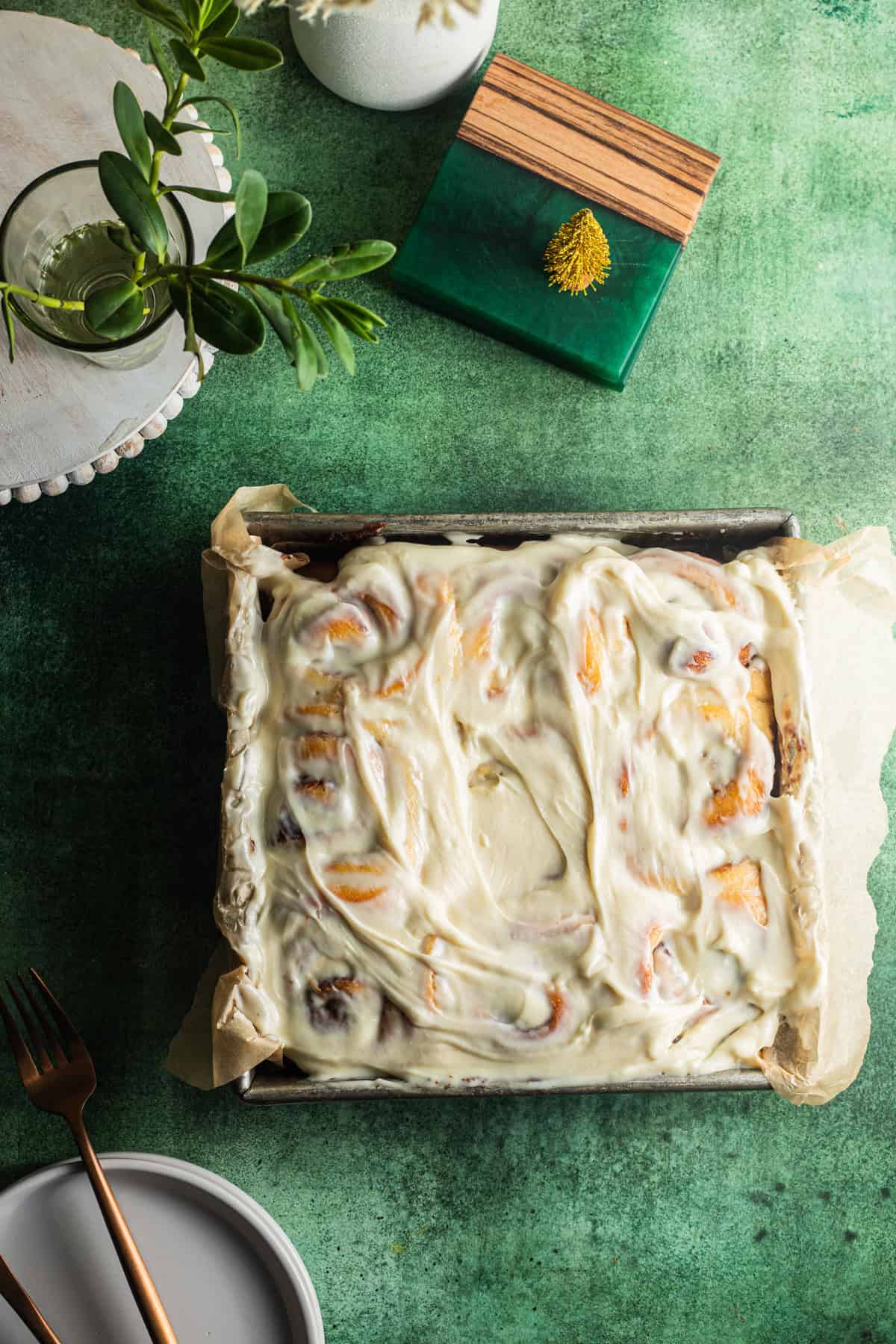 Cinnamon rolls in a metal baking pan with various holiday decorations in the background.