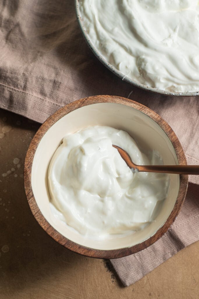A wooden bowl of yogurt with a large bowl of yogurt in the background.