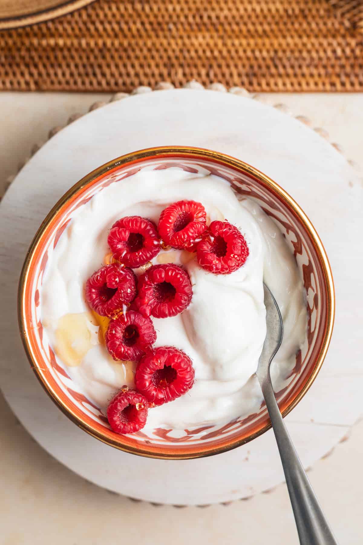 A bowl of homemade Greek yogurt topped with raspberries and honey.