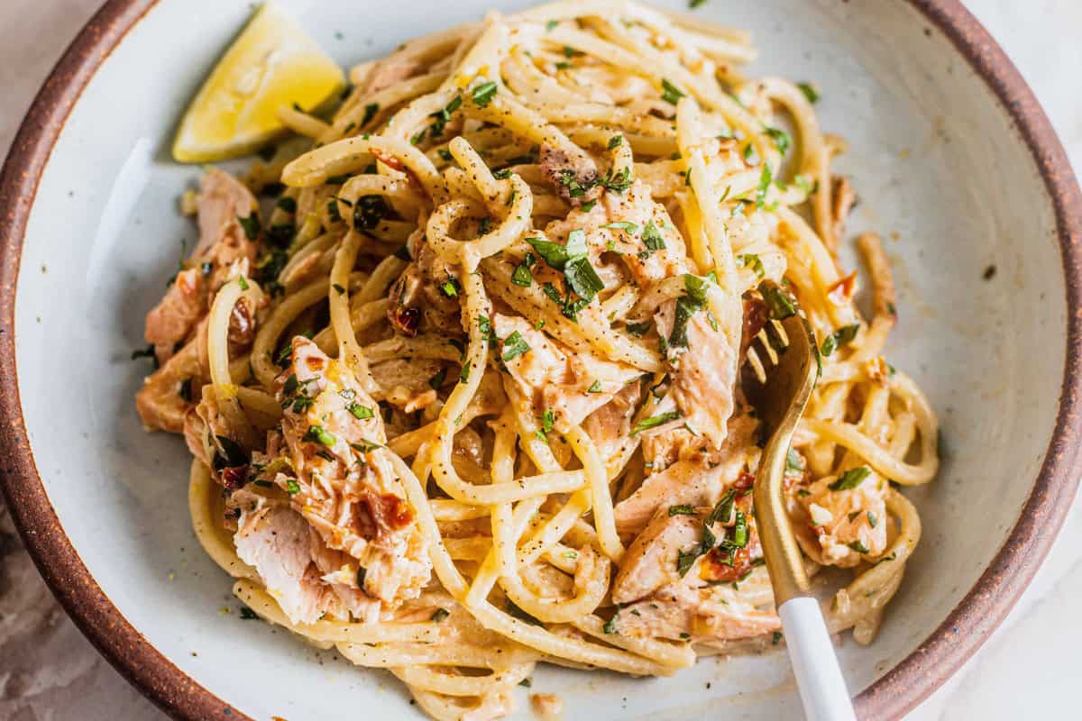 A plate of salmon pasta coated in a yogurt sauce with chunks of salmon, lemon, and fresh herbs.