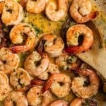 A dutch oven with cooked shrimp in a butter sauce with a wooden spoon.