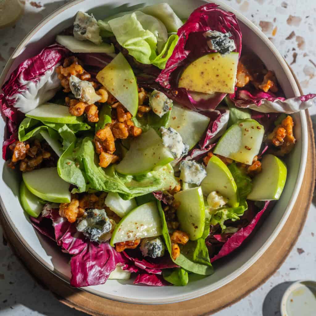 A bowl of salad with radicchio, lettuce, crumbled blue cheese, walnuts and apples drizzled with a mustard dressing.