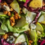 A bowl of lettuce, radicchio, apples, walnuts, and blue cheese drizzled with a mustard dressing.