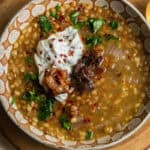 A bowl of barley lentil soup topped with yogurt, chili flakes, parsley, and onions.