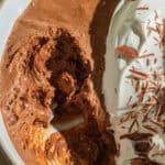 A bowl of chocolate mousse with some taken out and whipped cream on top.