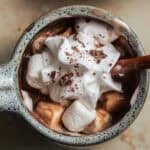 A ceramic mug of hot chocolate topped with melting whipped cream, shaved chocolate, and mini marshmallows.