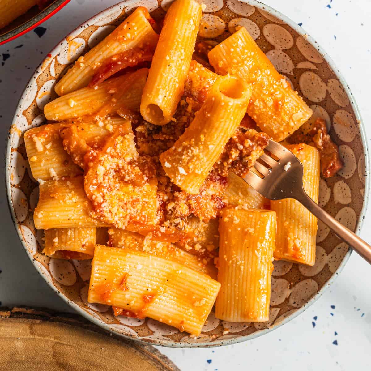 A bowl of rigatoni in a tomato sauce with grated cheese and a fork.