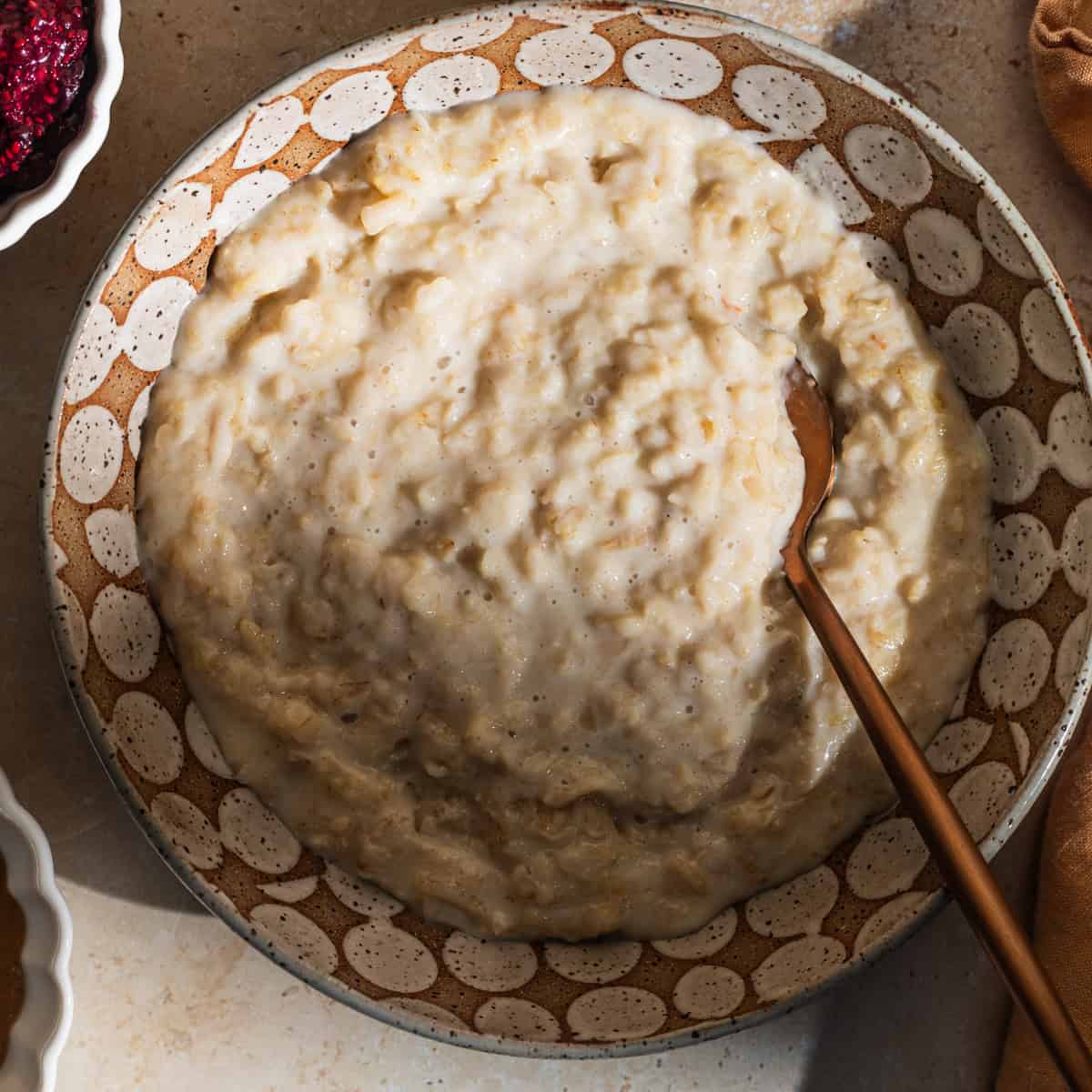 A bowl of oatmeal with a spoon in it and various bowls of ingredients in the background.