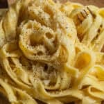 A plate of fettuccine alfredo topped with parmesan cheese and black pepper with a fork in the background.