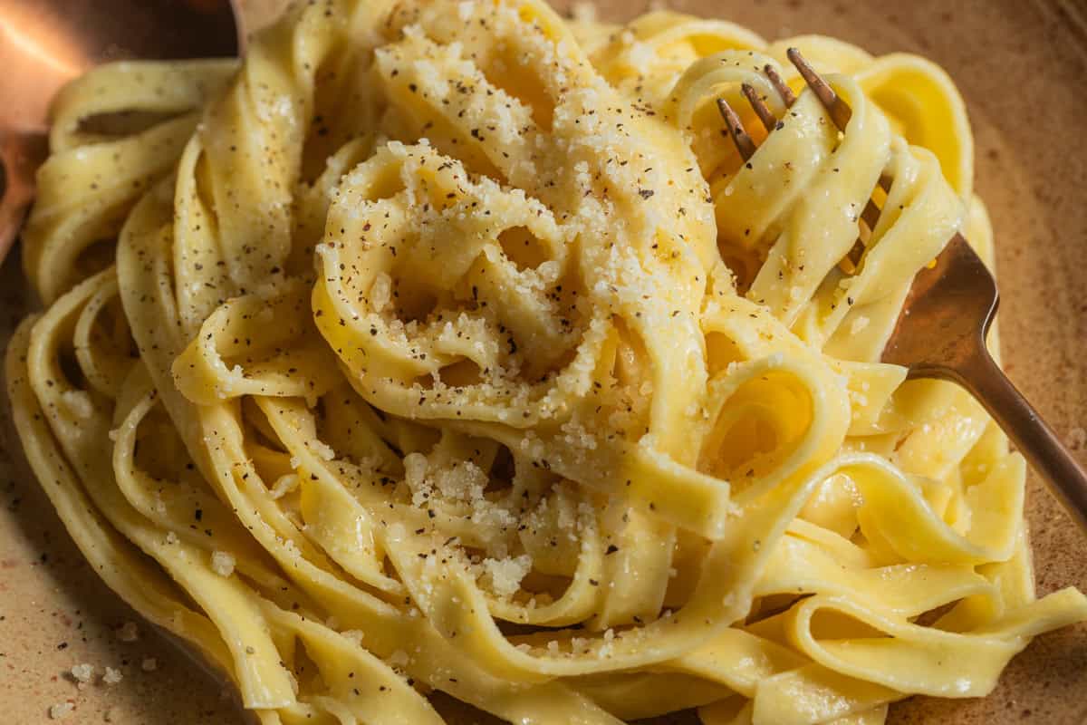 A plate of fettuccine alfredo topped with parmesan cheese and black pepper with a fork in the background.