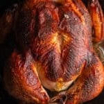 A cast-iron pan with a whole-roasted deeply browned chicken and pan drippings.