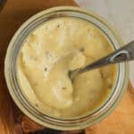 A jar of thick, creamy sauce dotted with black pepper with a spoon in it.
