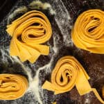 Various nests of pappardelle pasta on a semolina-dusted baking sheet.