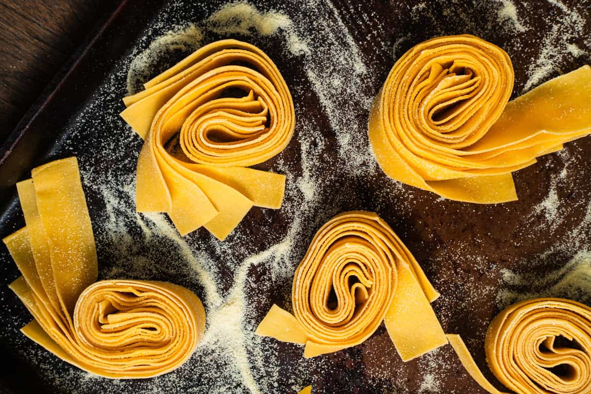 Various nests of pappardelle pasta on a semolina-dusted baking sheet.