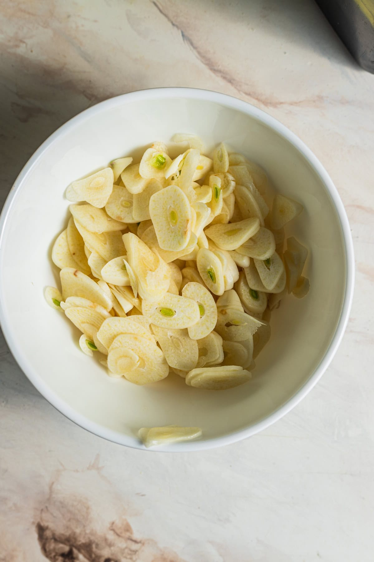 A bowl of thinly sliced garlic on a countertop.
