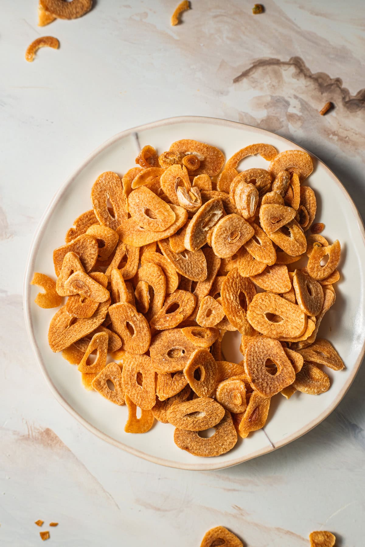 A plate of crispy fried garlic chips with more garlic chips on the countertop in the background.