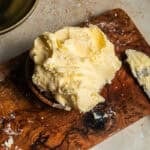A cutting board with a heap of softened butter next to a knife with butter.