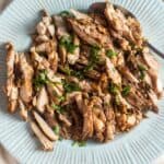 A plate of chicken shawarma topped with herbs on a linen napkin.