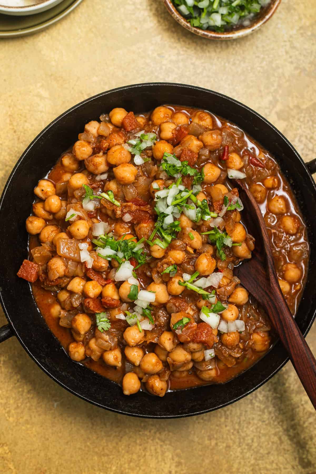 A kadai with a tomato-based chickpea curry topped with fresh onion and cilantro.