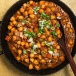 A kadai with chickpeas in a tomato sauce topped with onions and fresh cilantro.