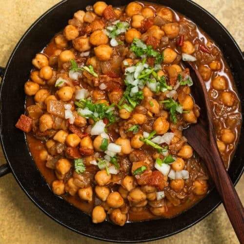 A kadai with chickpeas in a tomato sauce topped with onions and fresh cilantro.