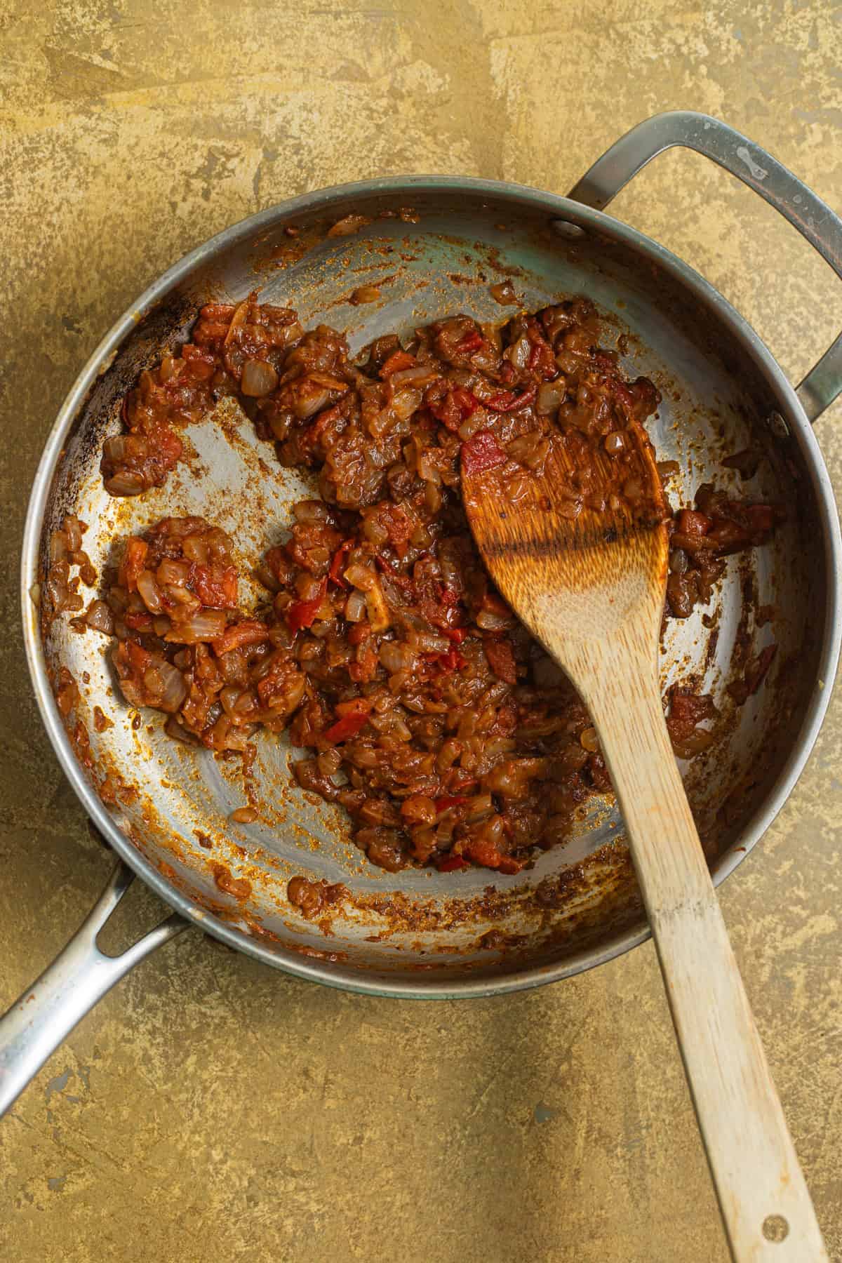 A stainless steel skillet with a mixture of tomatoes and onions browned in a skillet.