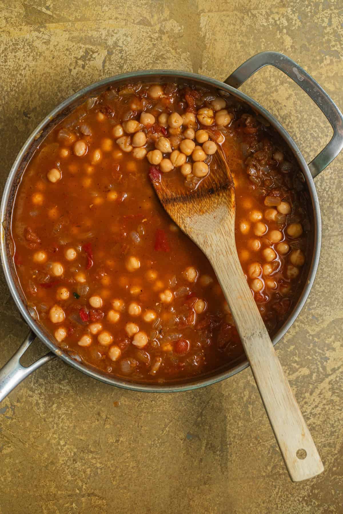 A stainless steel skillet with chickpeas in a tomato curry.