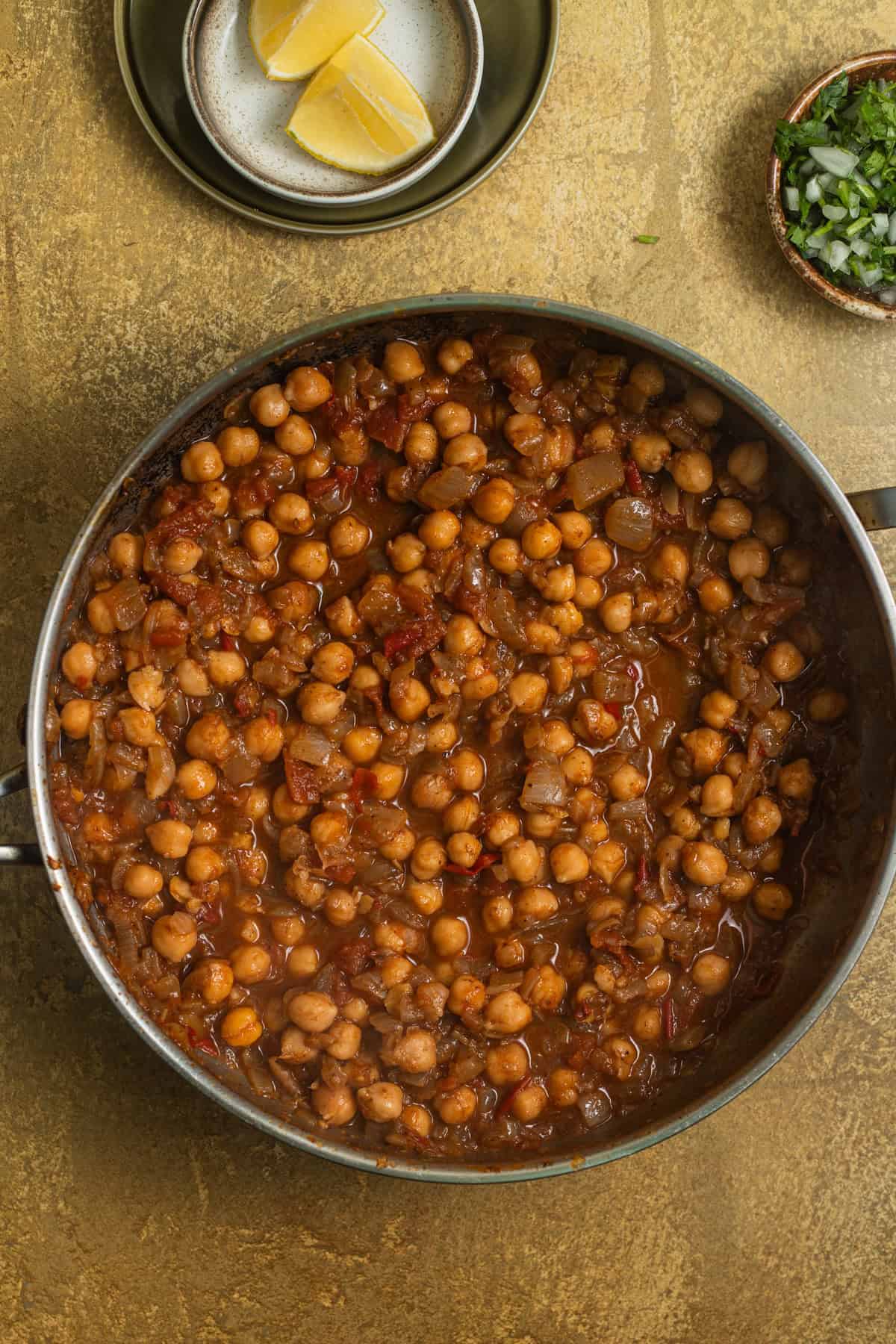 A stainless steel skillet with chickpea tomato curry and toppings in the background.