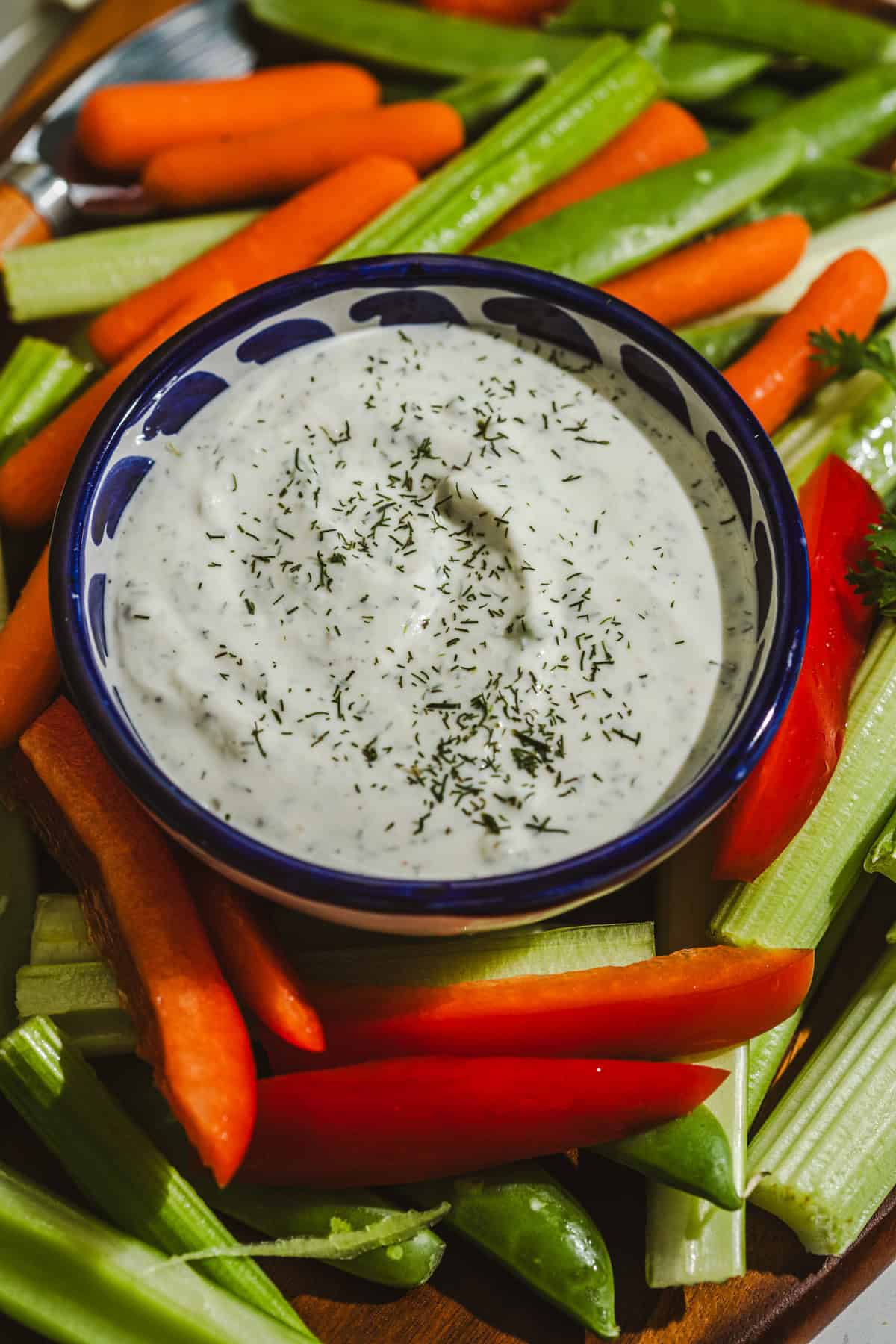 A bowl of ranch dressing topped with fresh herbs surrounded by crudites.
