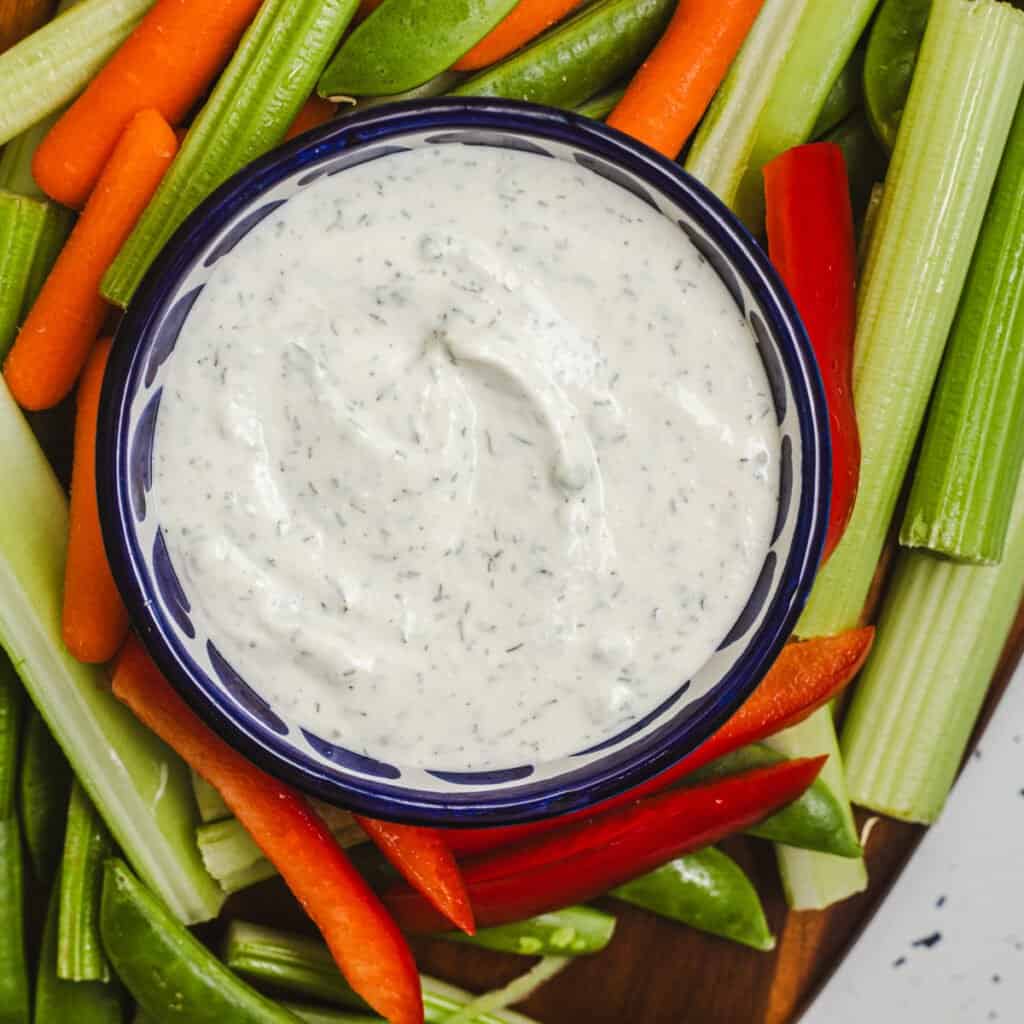 A bowl of Greek yogurt ranch with herbs surrounded by crudites on a platter.