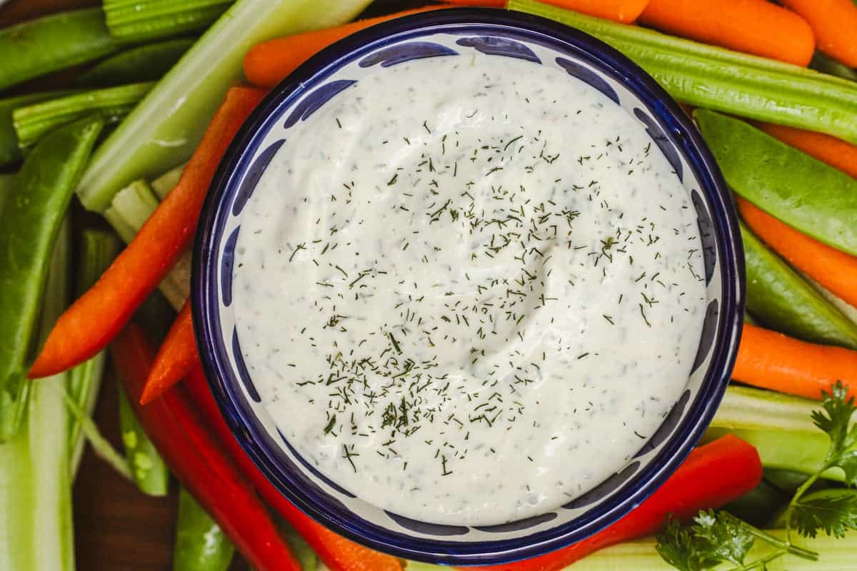 A bowl of Greek yogurt ranch dressing surrounded by various cut up vegetables.