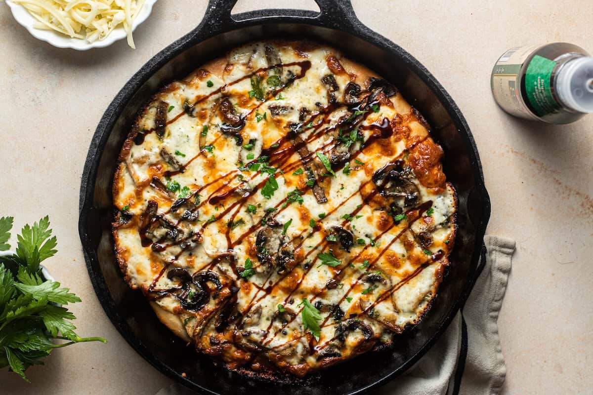 A pan pizza in a cast-iron skillet topped with balsamic glaze, herbs, and mushrooms.
