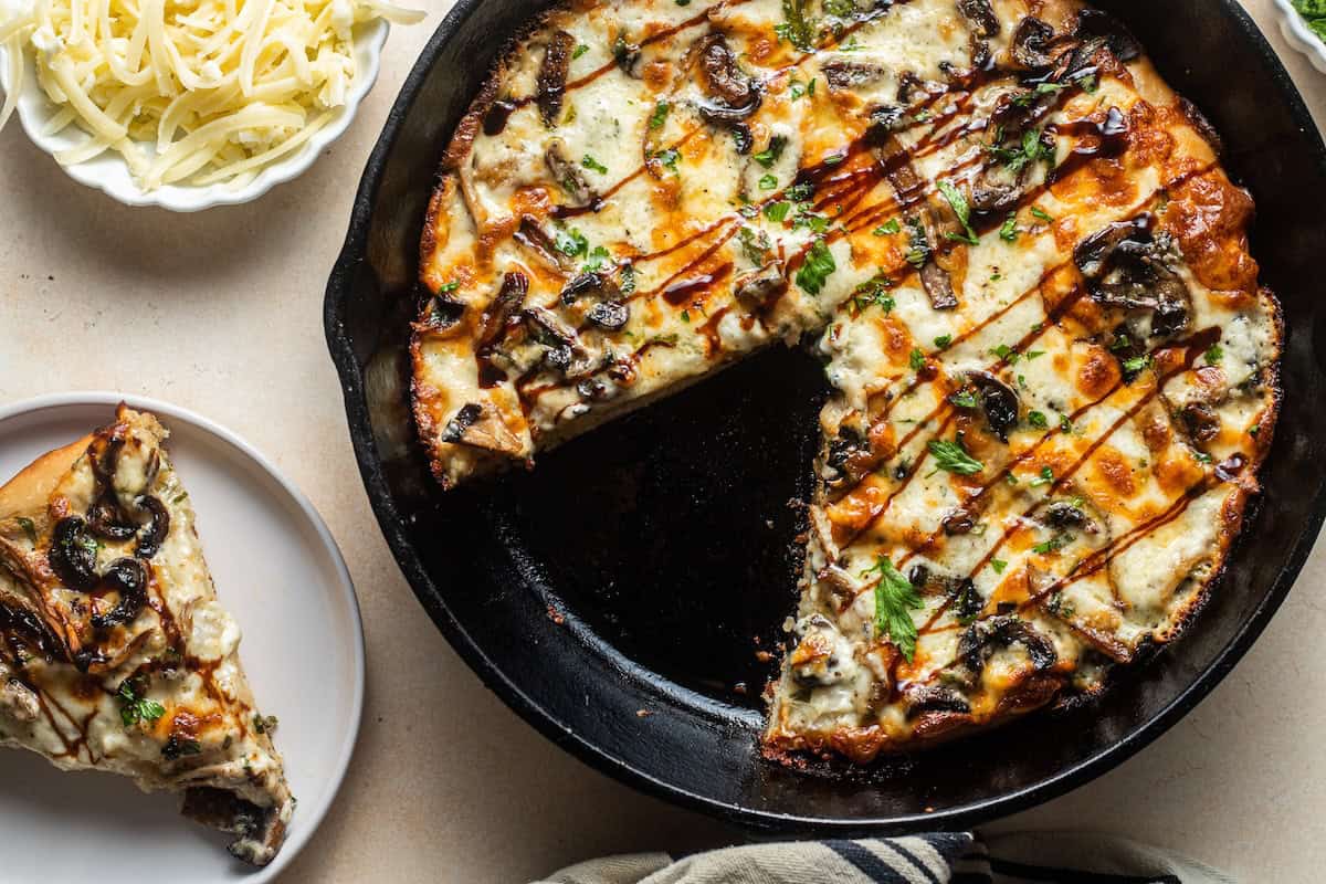 A pan pizza in a cast-iron skillet with a piece taken out and put on a plate next to it.