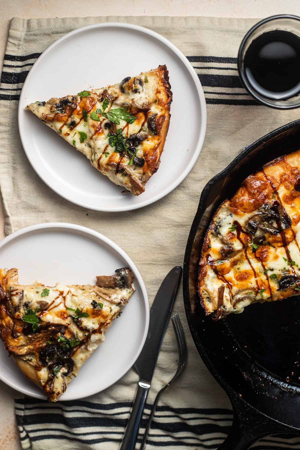 Two slices of mushroom pizza on plates next to a cast-iron skillet with pizza.