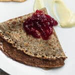 A buckwheat crepe on a plate folded into a triangle topped with jam and brie cheese.