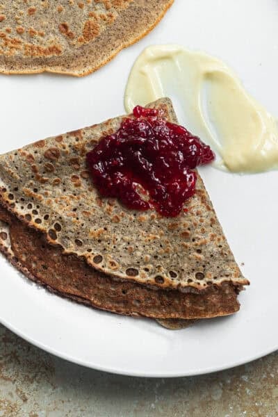 A buckwheat crepe on a plate folded into a triangle topped with jam and brie cheese.