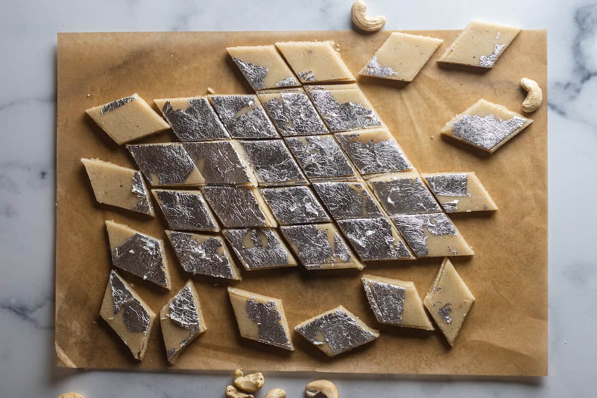 Silver vark decorated kaju katli pieces on a piece of parchment paper.
