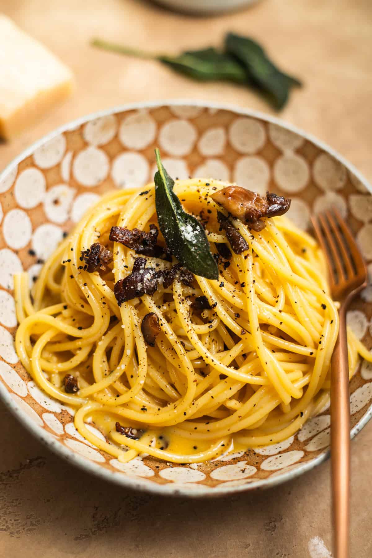 A bowl of spaghetti tossed in a carbonara sauce topped with mushrooms and sage.