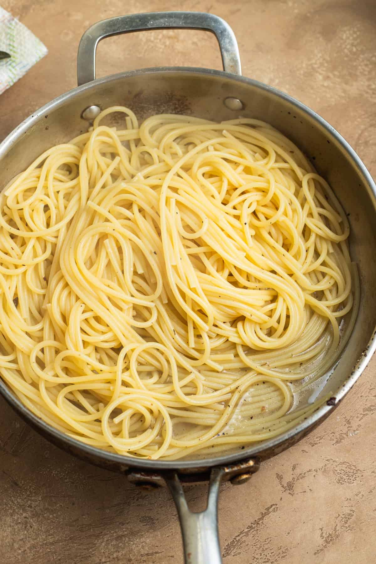 A stainless steel skillet with spaghetti in pasta water.