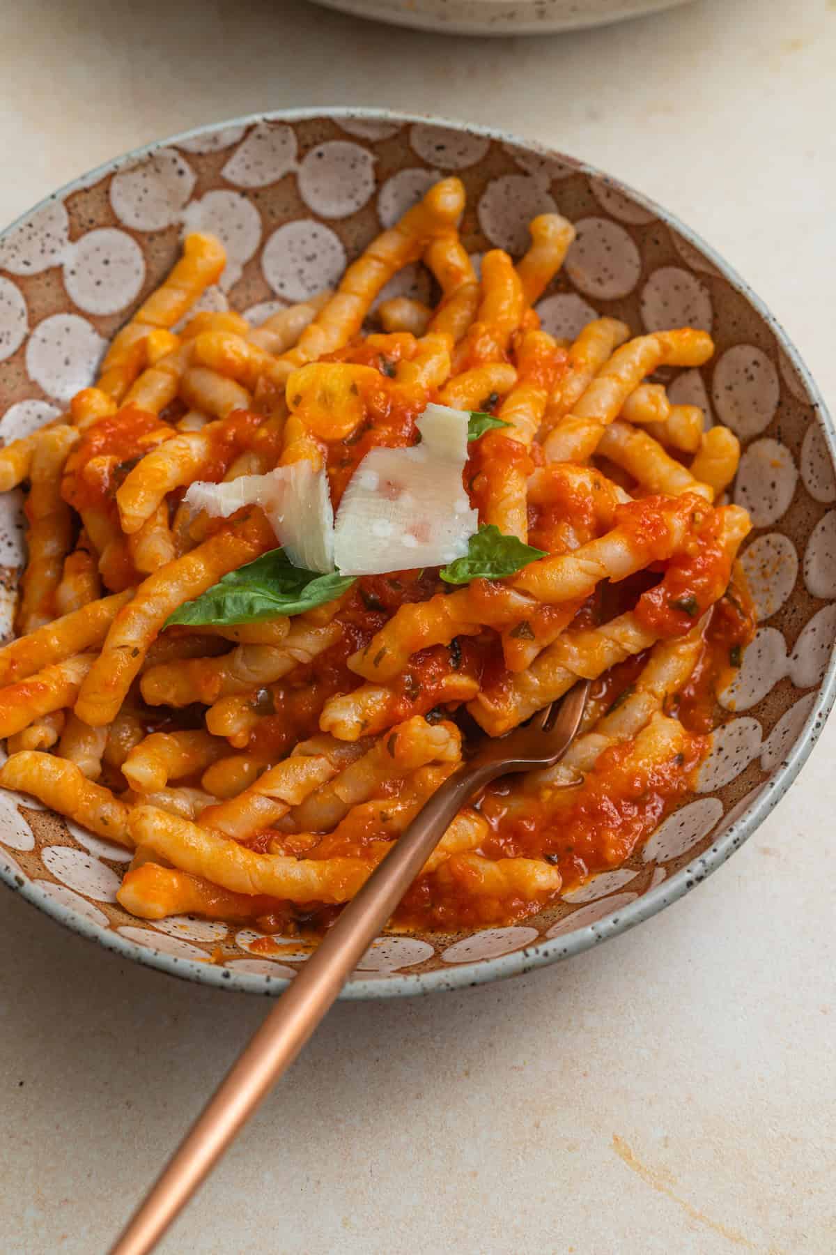 A bowl of busiate pasta tossed in a tomato sauce and garnished with shaved parmigiano-reggiano cheese and basil leaves.