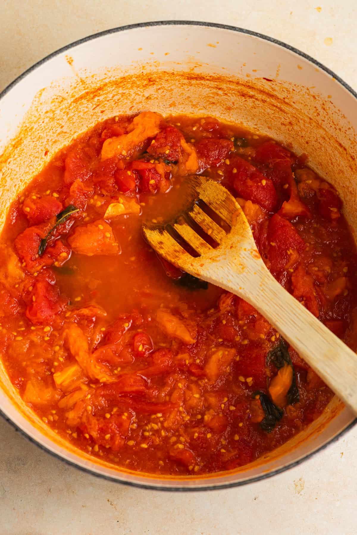 Stewed chopped tomatoes in a dutch oven with a wooden spoon.