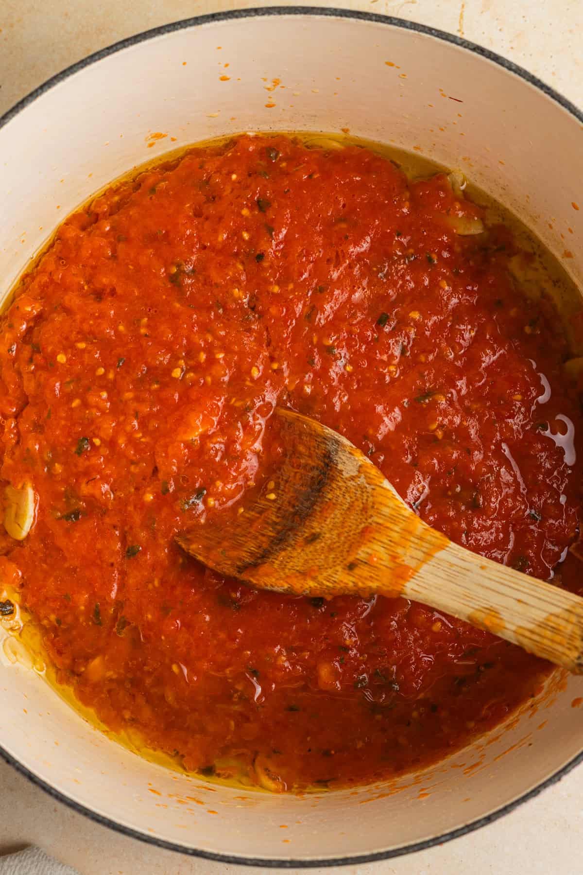 Tomato sauce with specks of basil and garlic in a dutch oven with a wooden spoon.