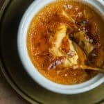 A spoon in a ramekin of maple creme brulee on a plate.