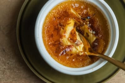 A spoon in a ramekin of maple creme brulee on a plate.