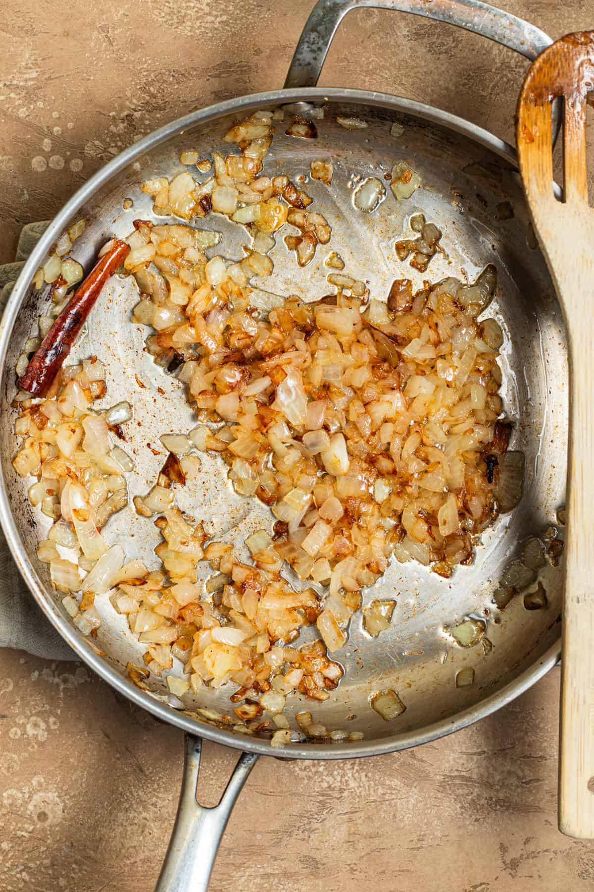 A stainless steel skillet with sauteed onions and a wooden spoon on top.